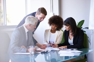 two women two men clustered at desk teamwork, midfield, gray